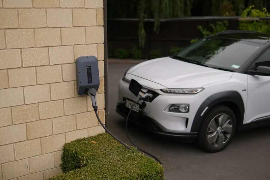 Wall-mounted EV charger on a brick wall charging a car in a driveway