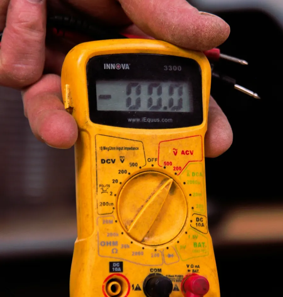 Yellow multimeter with test leads held in a hand